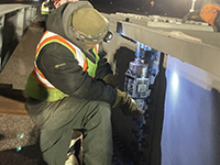 Worker uses a powered ratchet to install bolts on bridge beam.